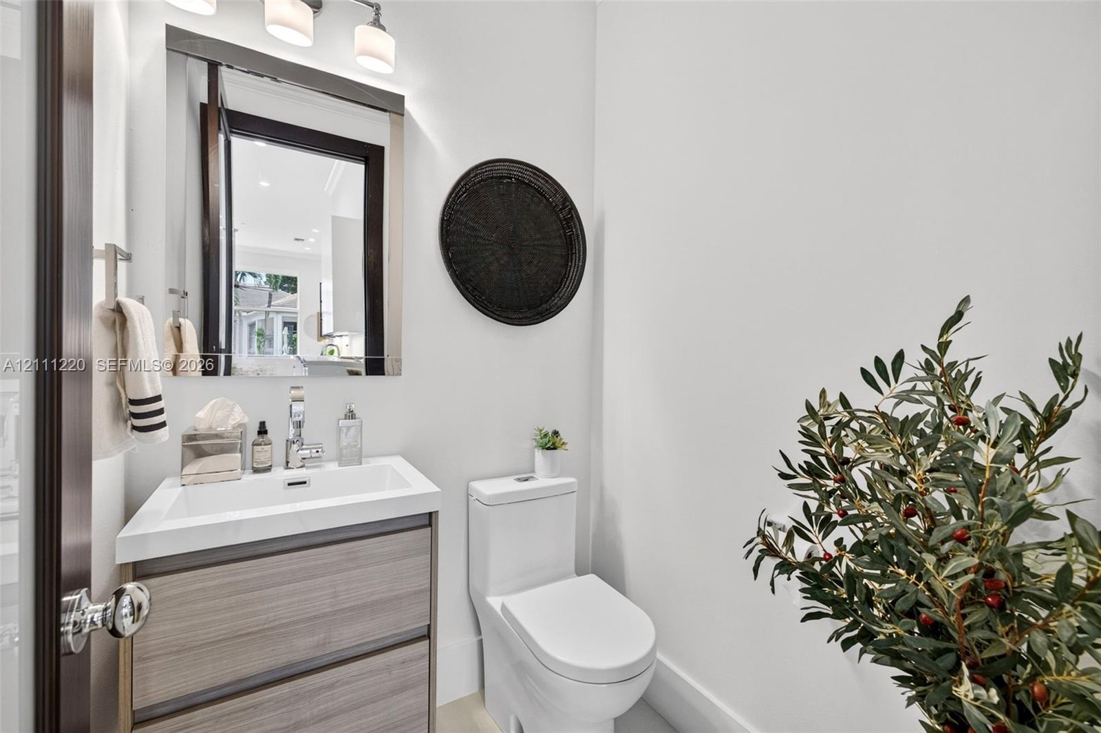Vanity with a rectangular basin, wood-finish cabinetry, wall-mounted mirror, three-light fixture, and dual-flush toilet