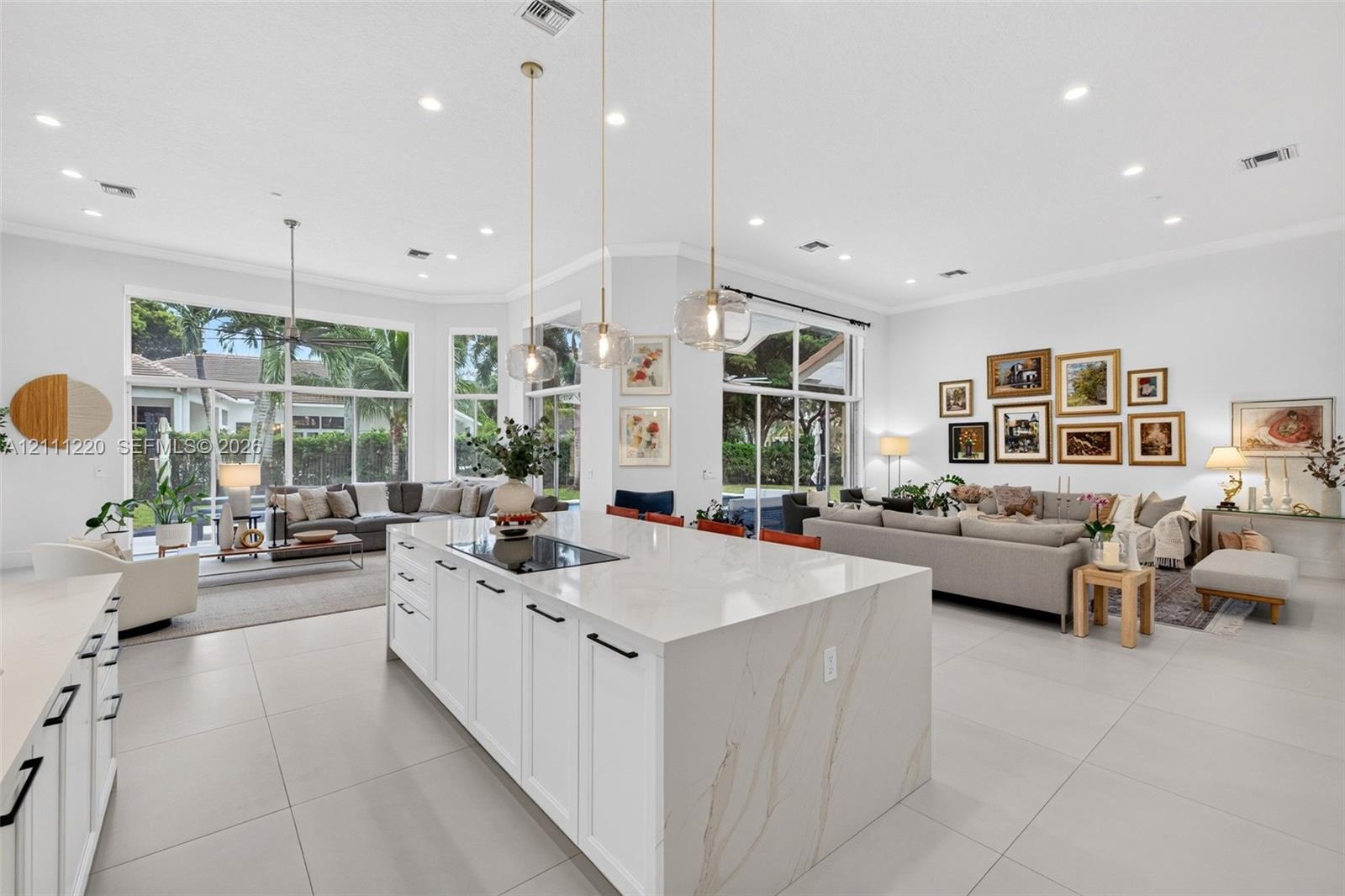 Large kitchen island with a stone-finish waterfall countertop, integrated cooktop, white shaker-style cabinetry, matte black hardware, and three glass pendant lights