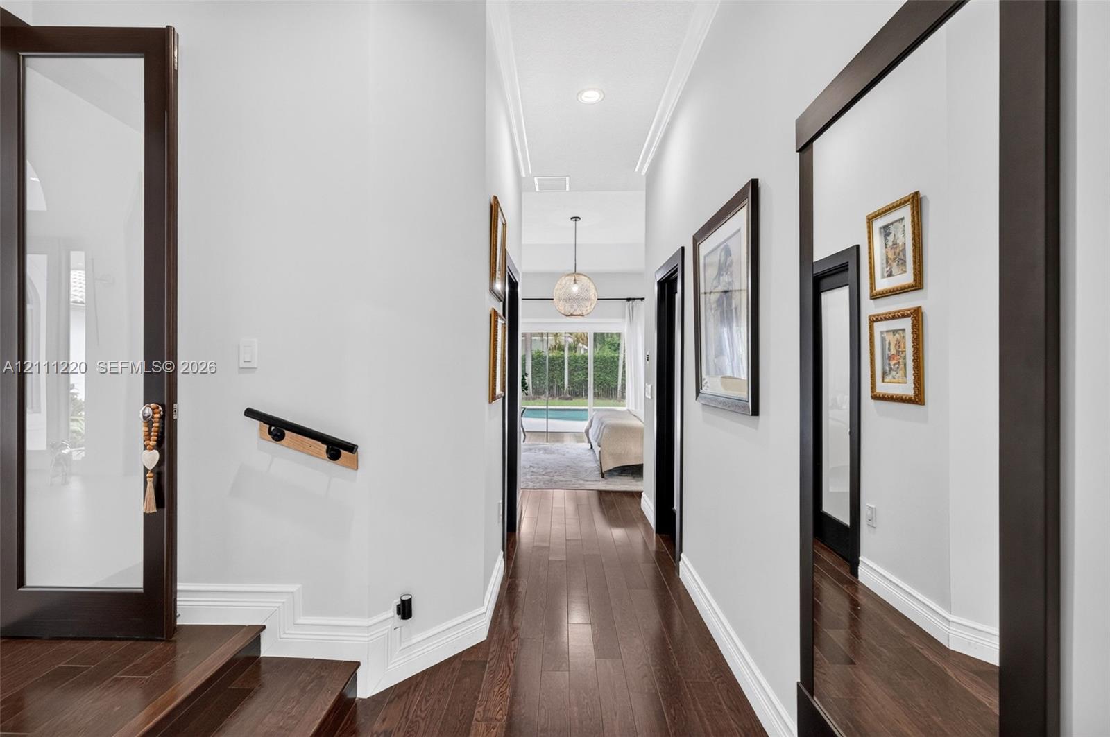 Hallway featuring dark wood-finish flooring, high ceilings with recessed lighting, crown molding, a decorative globe pendant fixture, and glass-paneled doors with dark frames