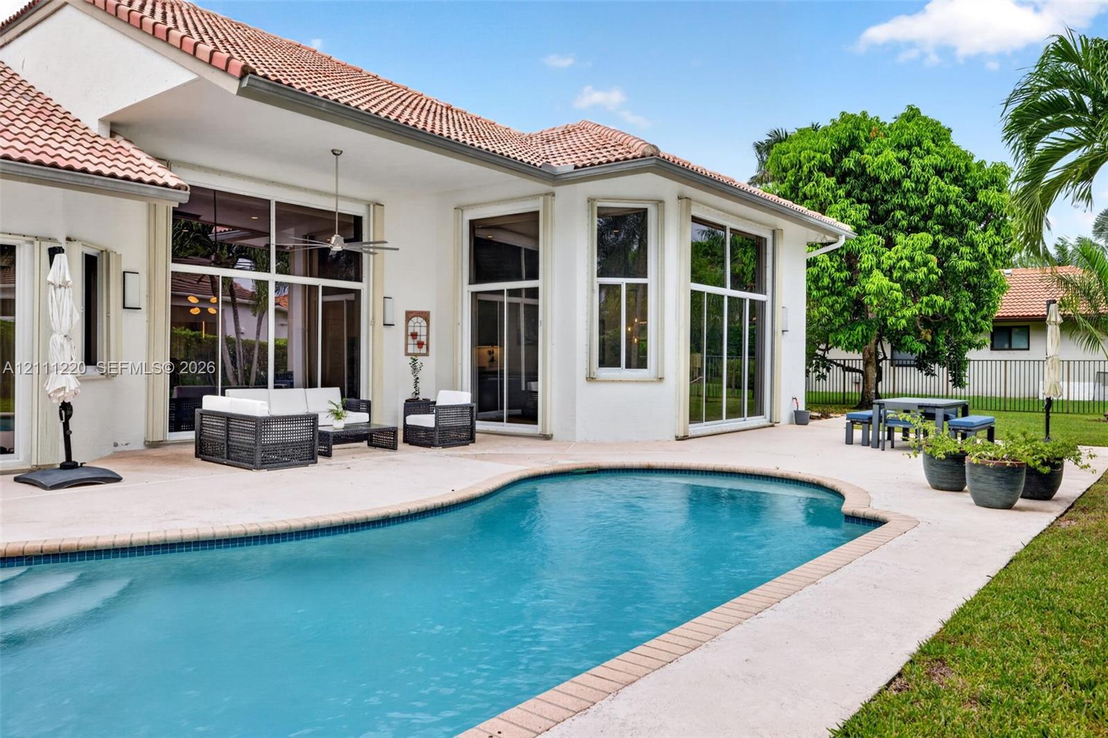 Stucco exterior featuring a clay tile roof, expansive concrete patio, and in-ground pool with stone coping
