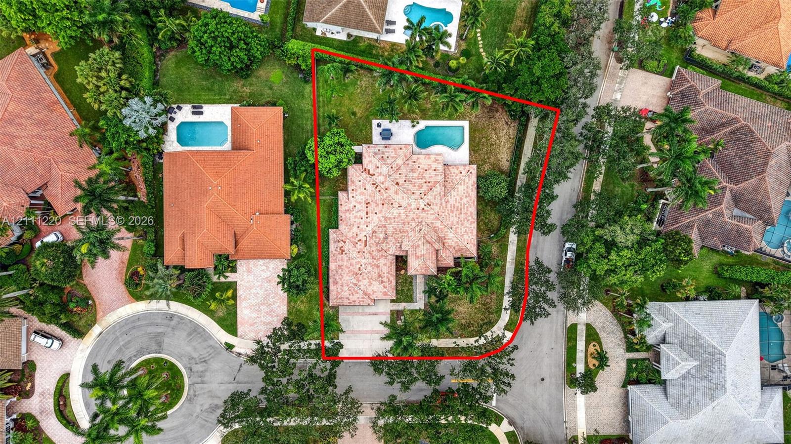 Aerial perspective of a property featuring a tiled roof, in-ground swimming pool, concrete driveway, and mature landscaping