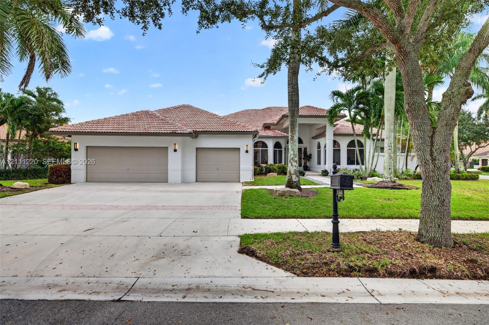 Stucco exterior featuring a multi-car garage, tiled roof, arched window detailing, and manicured landscaping