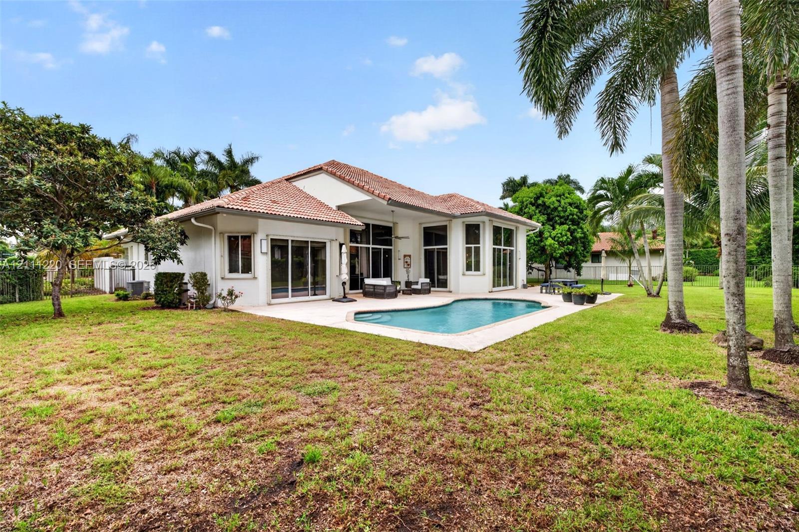 Stucco exterior featuring a clay tile roof, expansive concrete pool deck, in-ground swimming pool, and mature landscaping