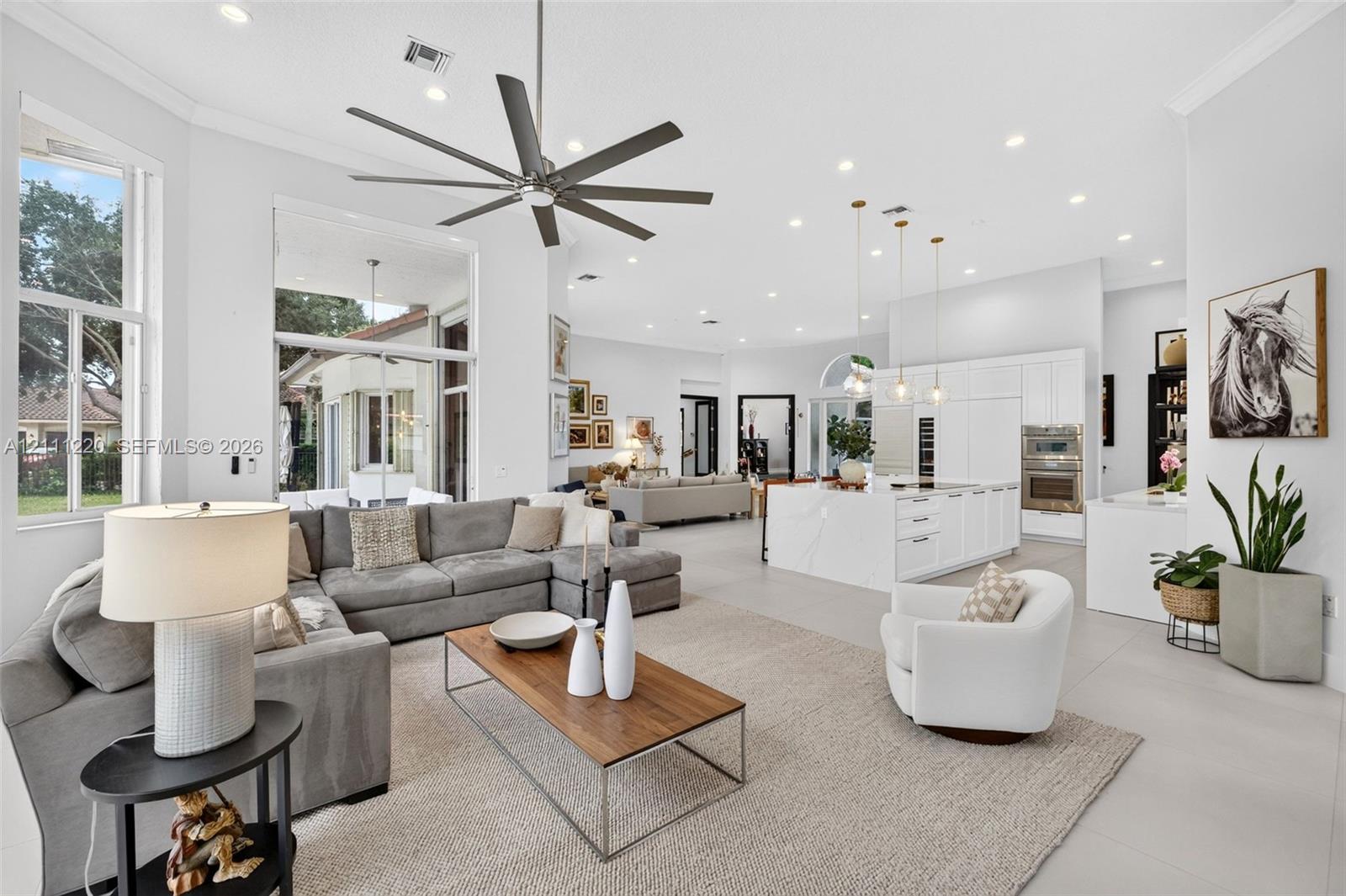 Open-concept living area featuring high ceilings, recessed lighting, large-format tile flooring, a chef's kitchen with a waterfall island, and a multi-blade ceiling fan