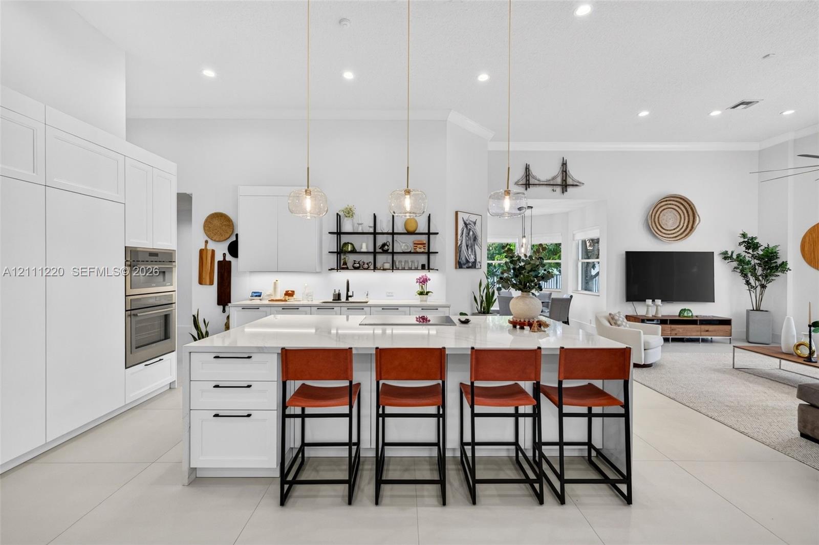 Kitchen featuring white shaker-style cabinetry, a large central island with a stone countertop, built-in stainless steel double ovens, recessed lighting, and three suspended glass pendant lights