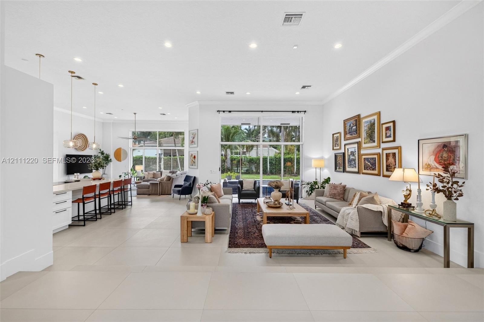 Open-concept living space featuring large-format tile flooring, recessed lighting, floor-to-ceiling glass windows, and a built-in kitchen island with pendant lighting