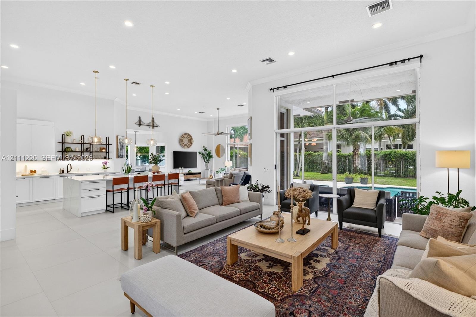 Open-concept living area featuring large-format tile flooring, high ceilings with recessed lighting, kitchen with white cabinetry and a center island, and floor-to-ceiling glass sliding doors