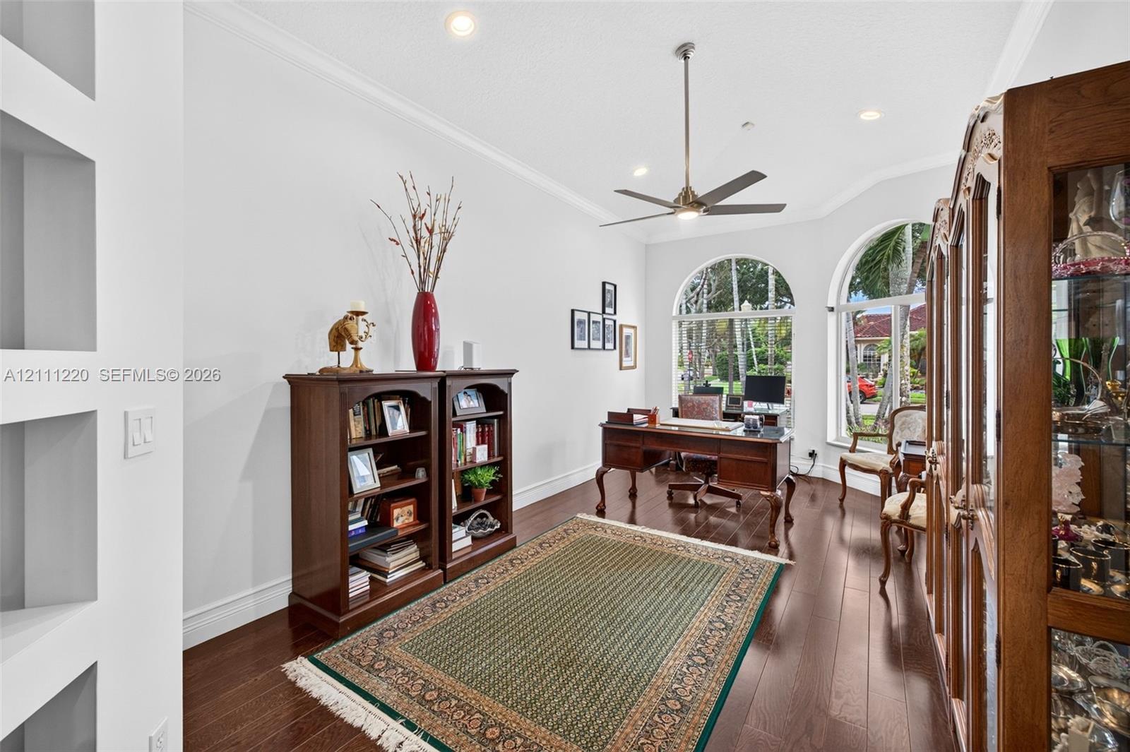 Room featuring wood-finish flooring, recessed lighting, crown molding, built-in wall niches, and arched windows