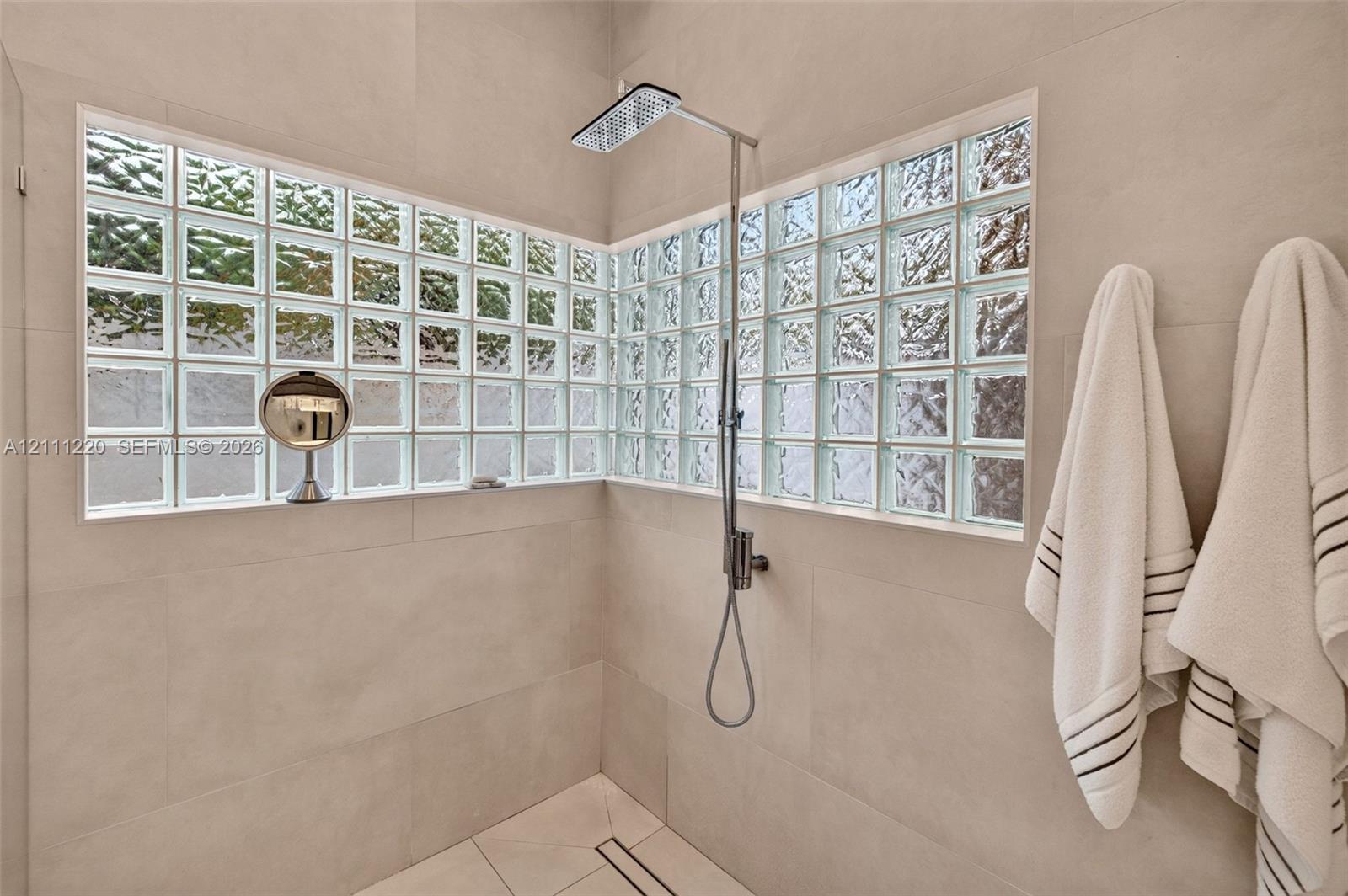 Walk-in shower featuring large-format wall tile, glass block windows, a rectangular rainfall shower head, and a linear floor drain