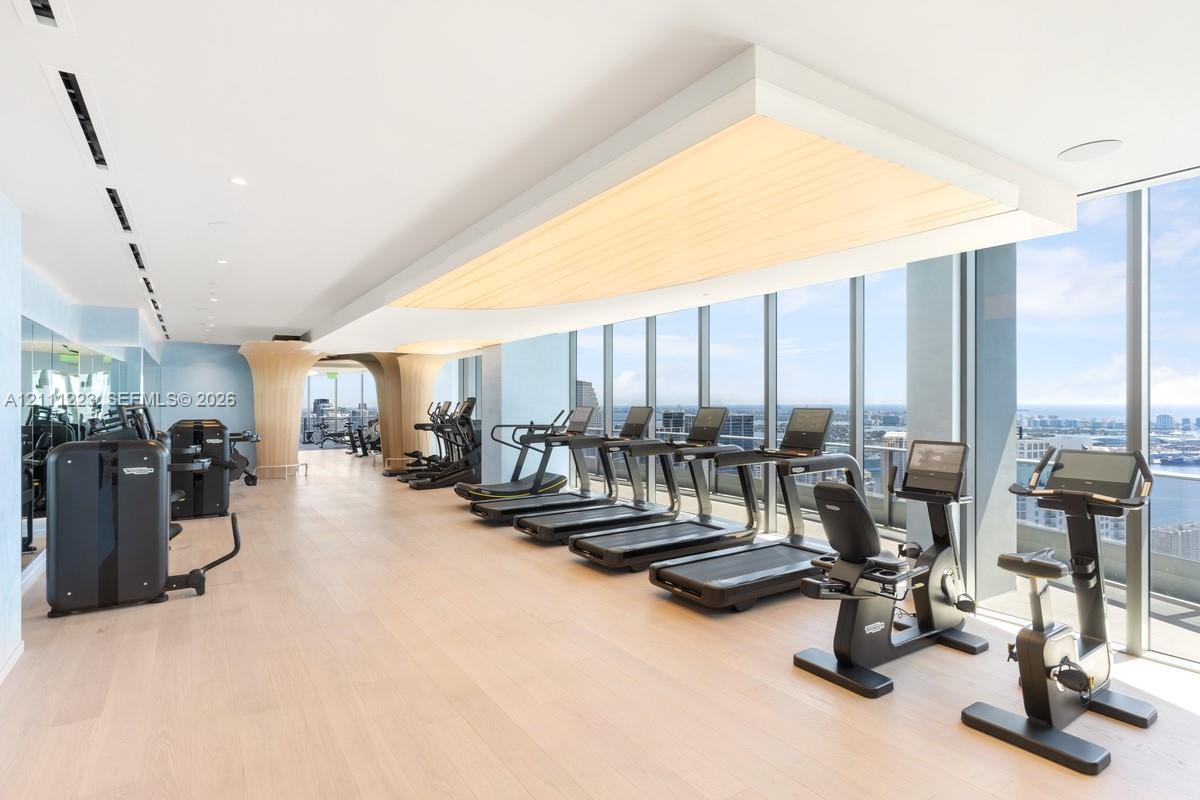 Fitness center featuring floor-to-ceiling windows, wood-finish flooring, custom architectural ceiling soffit with integrated lighting, and mirrored wall surfaces
