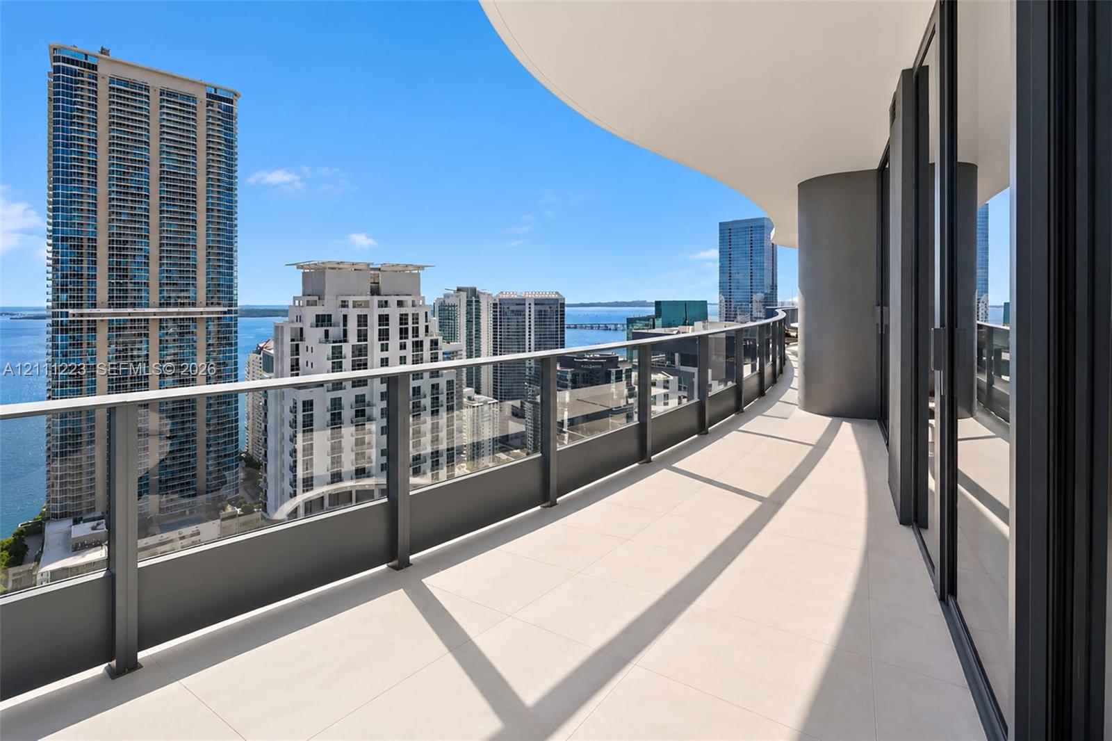 Curved balcony featuring light-toned tile flooring, glass panel railings with metal framing, and full-height sliding glass doors
