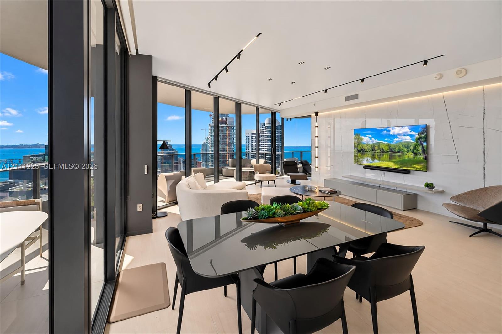 Floor-to-ceiling glass walls, large-format stone slab accent wall, recessed track lighting, and expansive exterior balcony