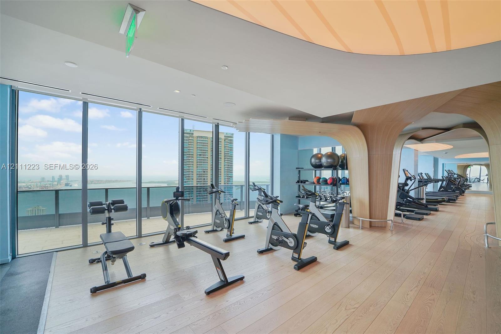Fitness center featuring floor-to-ceiling windows, wood-finish flooring, sculptural wood-veneer architectural accents, and recessed cove lighting