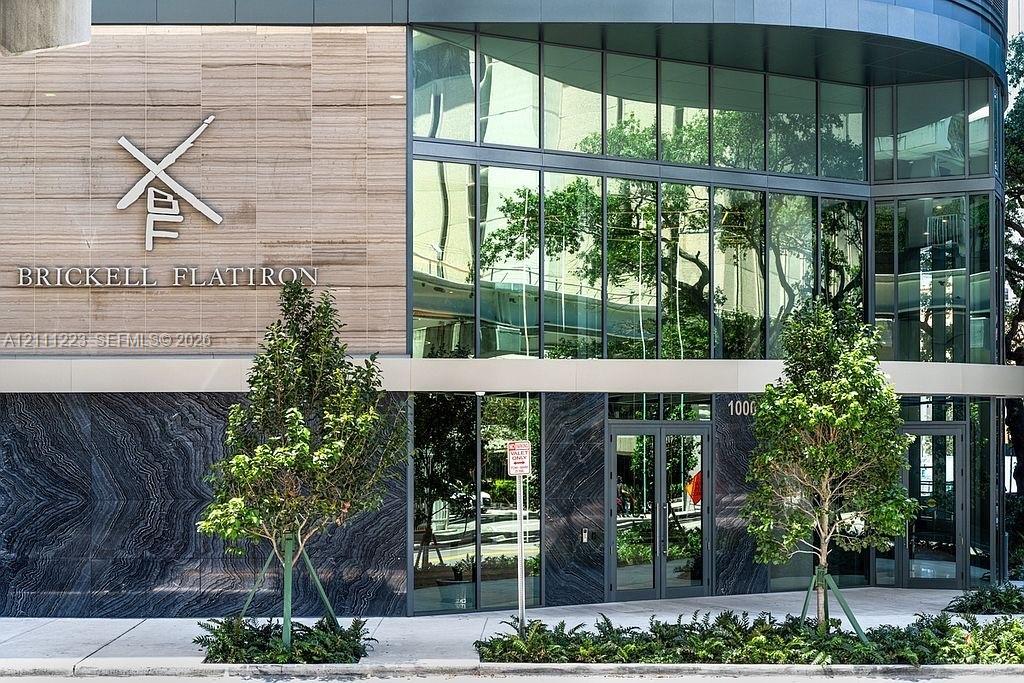 Contemporary high-rise facade featuring floor-to-ceiling glass paneling, stone tile exterior cladding, polished dark stone accents, and integrated entryway glass doors