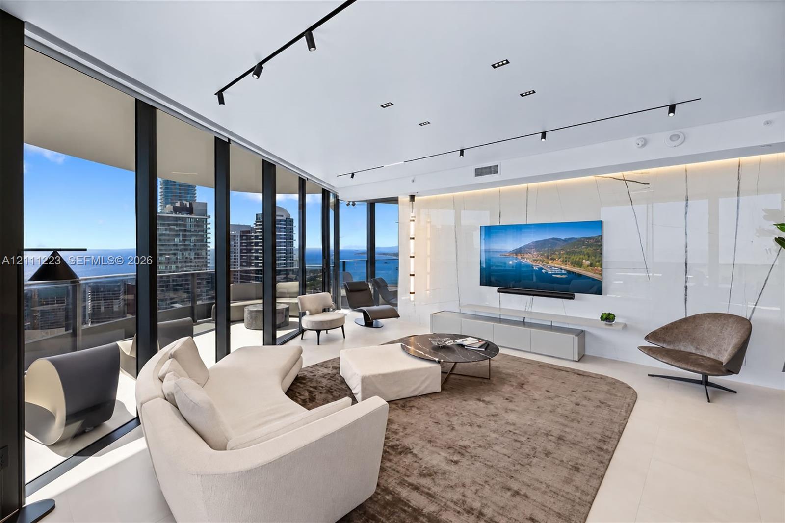 Floor-to-ceiling glass walls, large-format tile flooring, integrated track lighting, and a polished stone feature wall with a floating media console