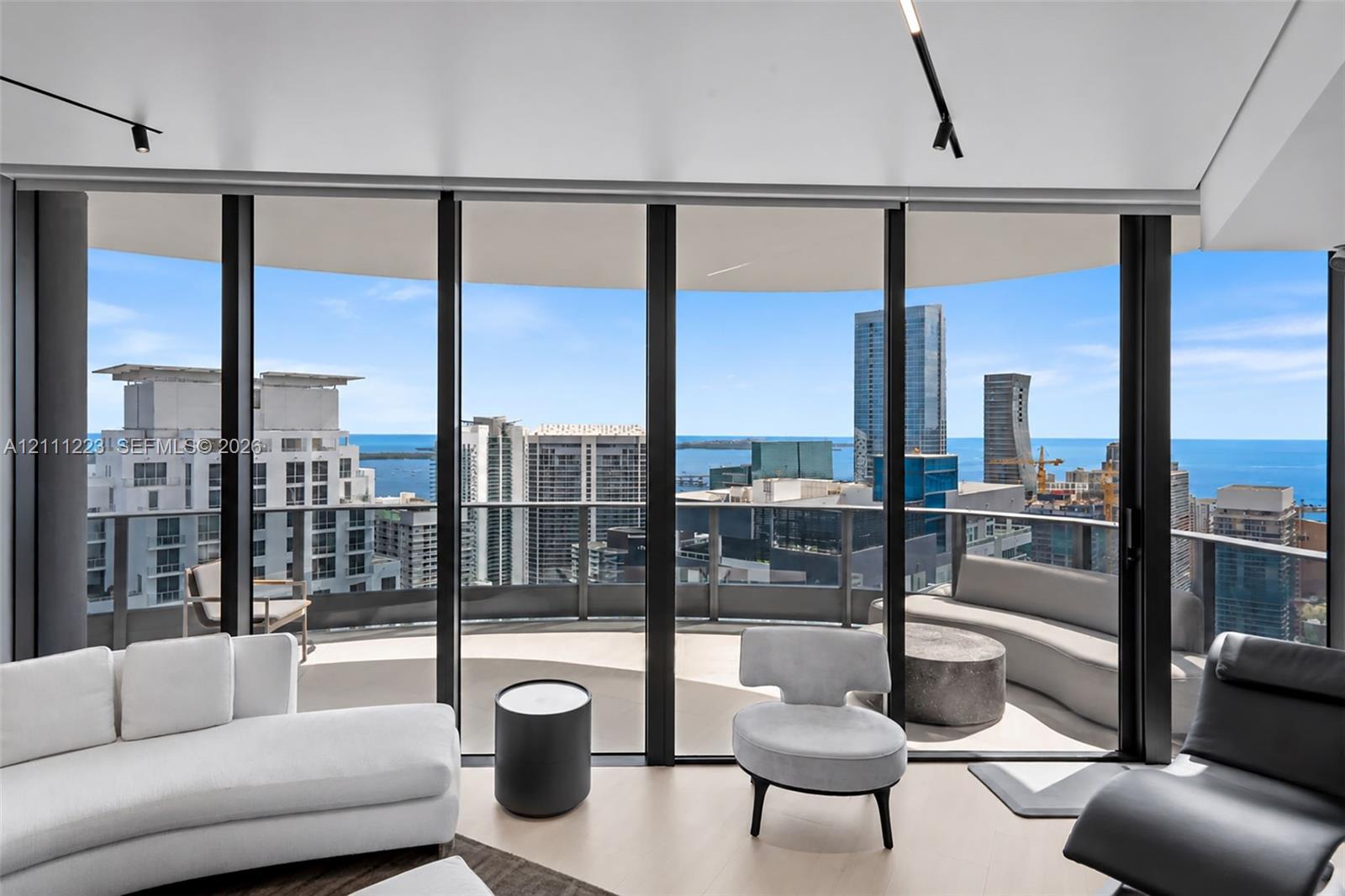 Floor-to-ceiling glass walls, curved balcony with structural glass railing, and wood-finish flooring