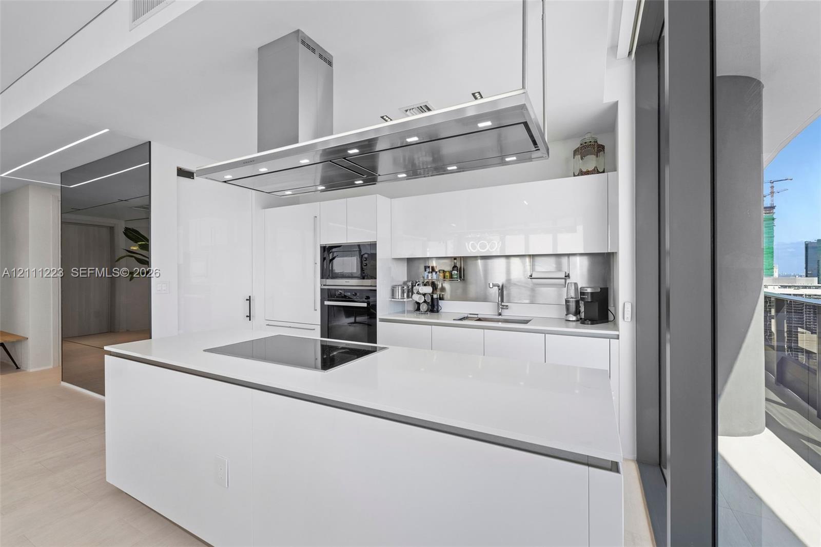 Kitchen featuring white gloss cabinetry, expansive island with integrated cooktop, stainless steel range hood, built-in wall oven, and metallic backsplash