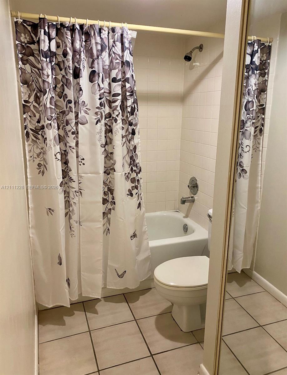 Full bathroom featuring a tub-shower combination with white wall tile, a standard porcelain toilet, and neutral tile flooring