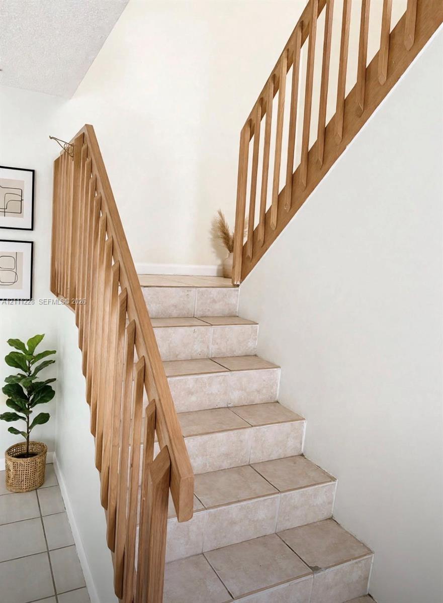 Staircase featuring tile treads and a light-toned wood-finish balustrade