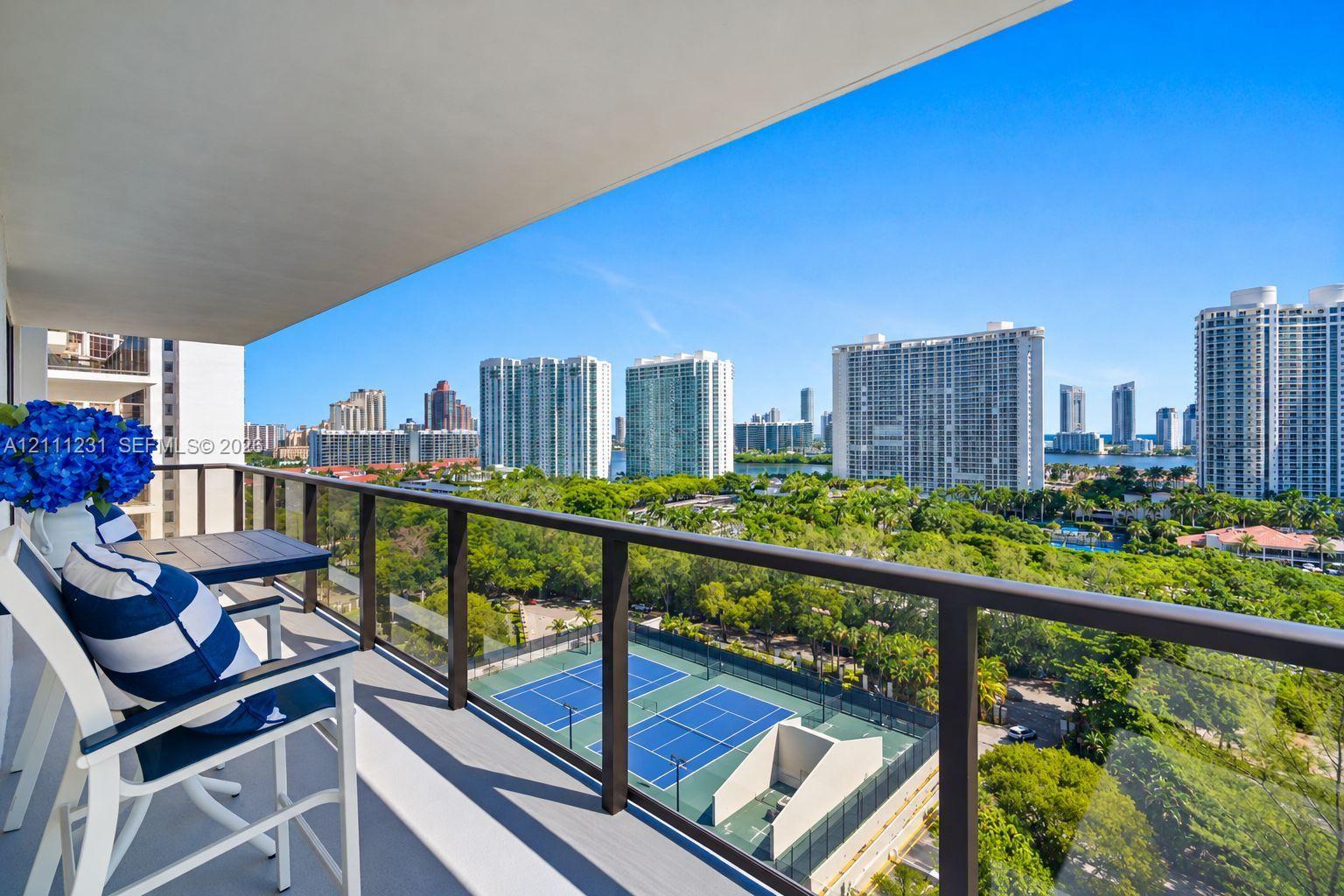 Covered private balcony featuring a glass and dark metal railing overlooking dual tennis courts and surrounding urban landscape Covered private balcony featuring a glass and dark metal railing overlooking dual tennis courts and surrounding urban landscape