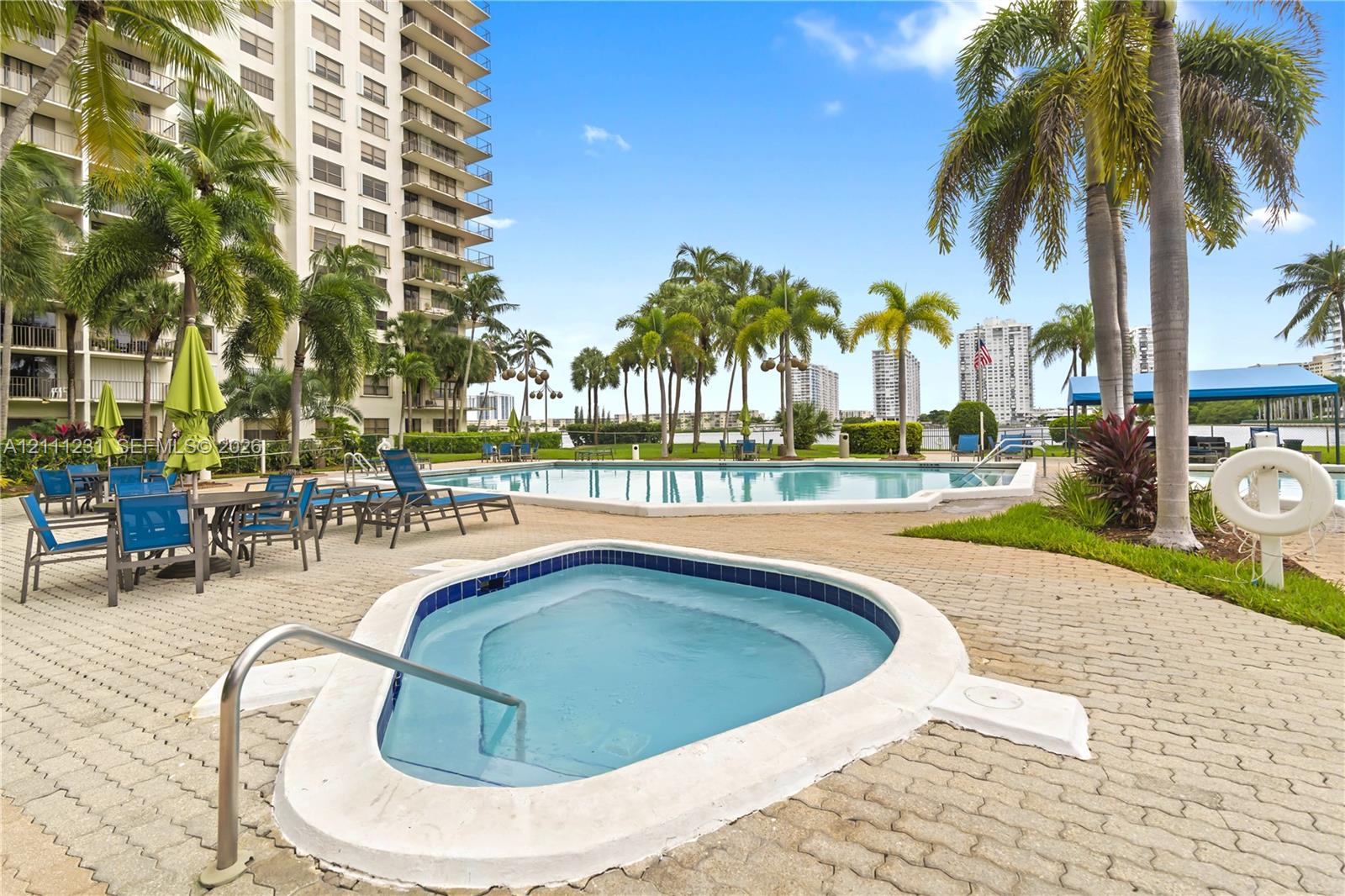 Outdoor pool and spa area featuring a paver deck, palm trees, and waterfront perimeter