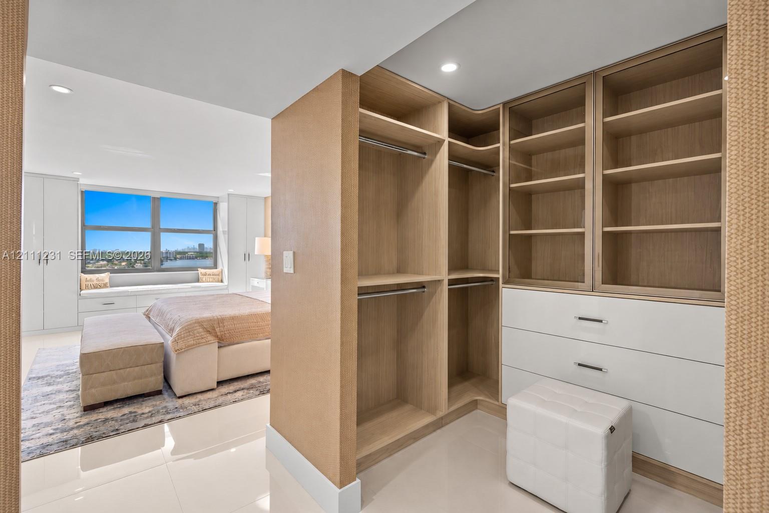 Custom walk-in closet featuring light wood-finish built-in shelving, hanging rods, and integrated white cabinetry with flat-panel drawers