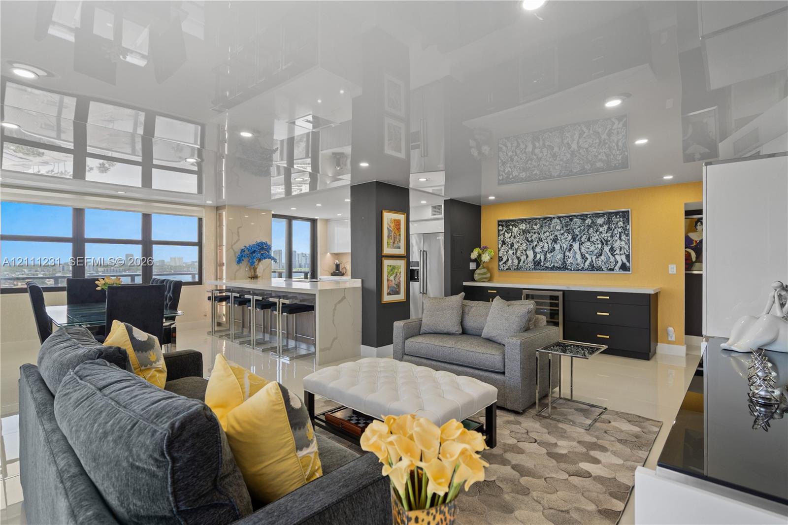 High-gloss reflective ceiling, wall-to-wall windows, large kitchen island with stone-finish waterfall edge, built-in cabinetry, and polished flooring