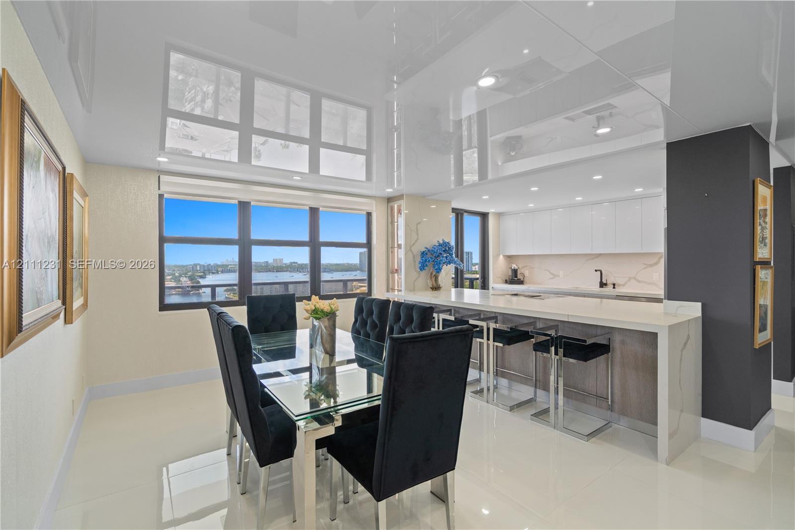 High-gloss ceiling with recessed lighting, expansive windows featuring water scenery, kitchen island with quartz-style countertop, slab backsplash, and flat-panel cabinetry