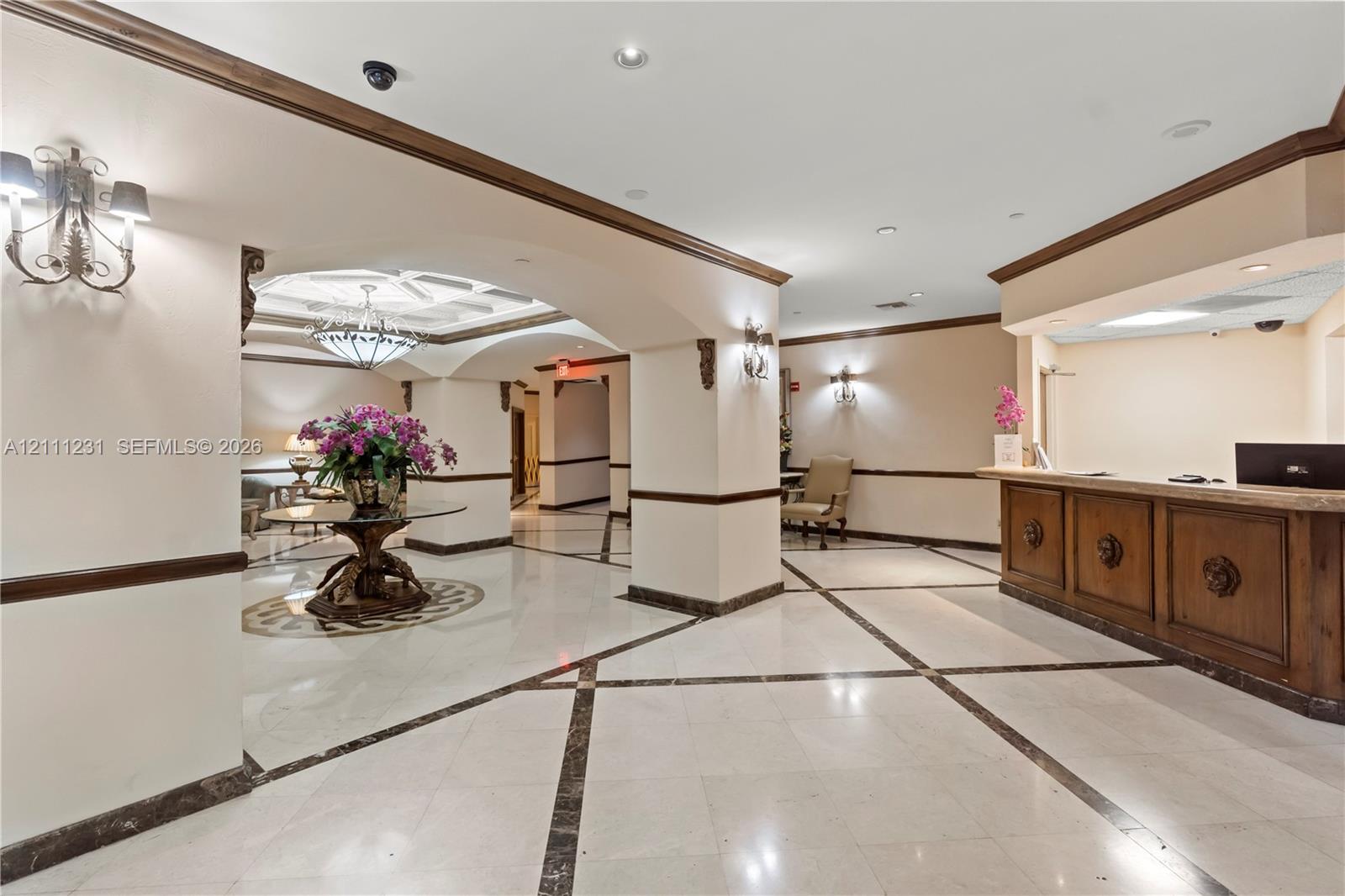 Lobby featuring arched architectural details, stone tile flooring with decorative inlay, built-in wooden reception desk, recessed lighting, and wall-mounted sconces