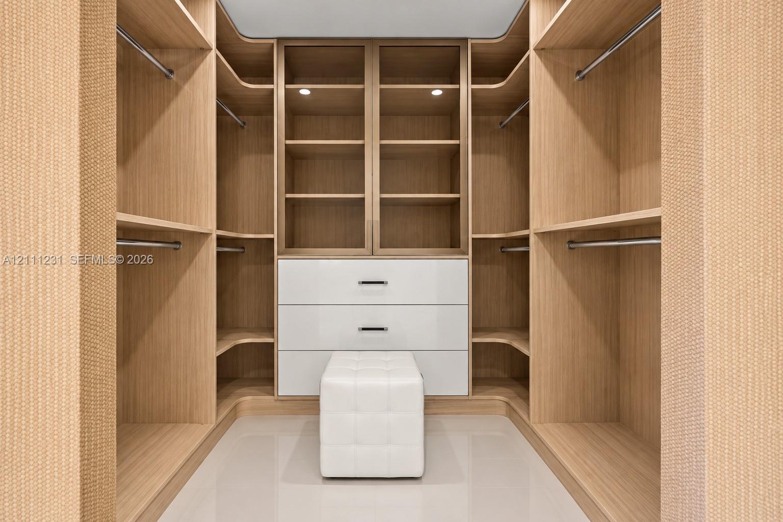 Custom closet featuring built-in wood-finish cabinetry, floor-to-ceiling shelving, integrated garment rods, and a white lacquer three-drawer storage unit