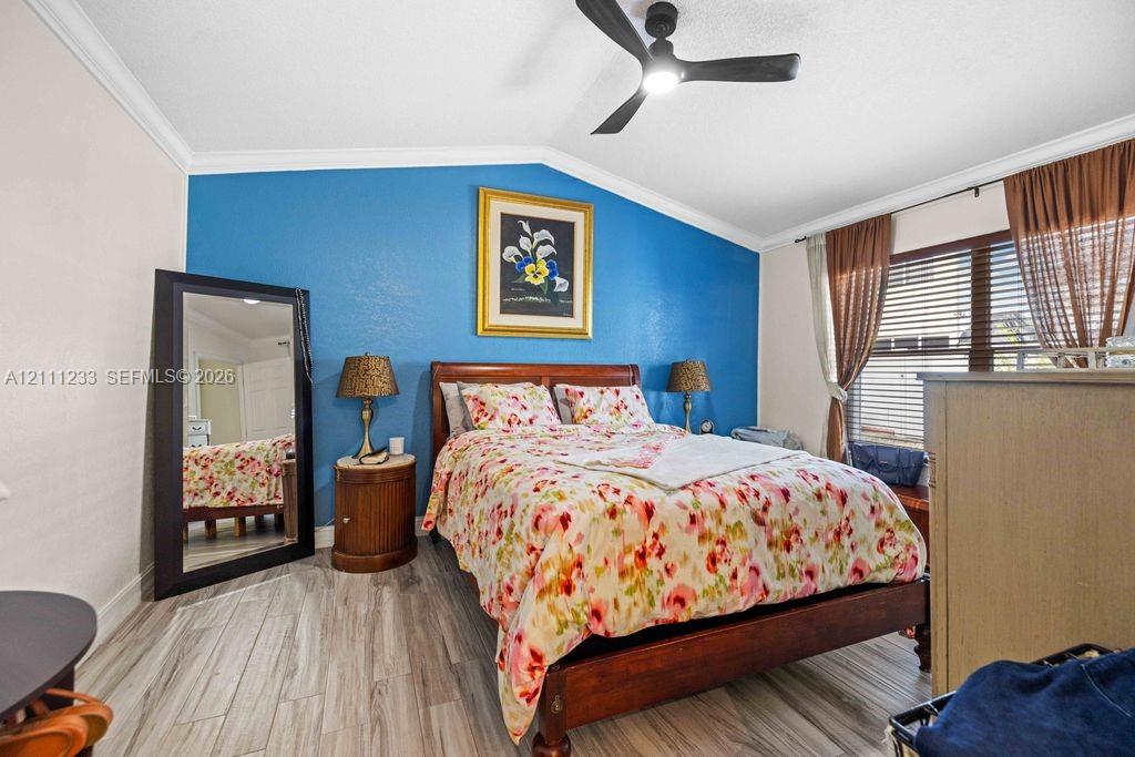 Vaulted ceiling featuring a matte black finish ceiling fan and crown molding, accented by wood-finish flooring