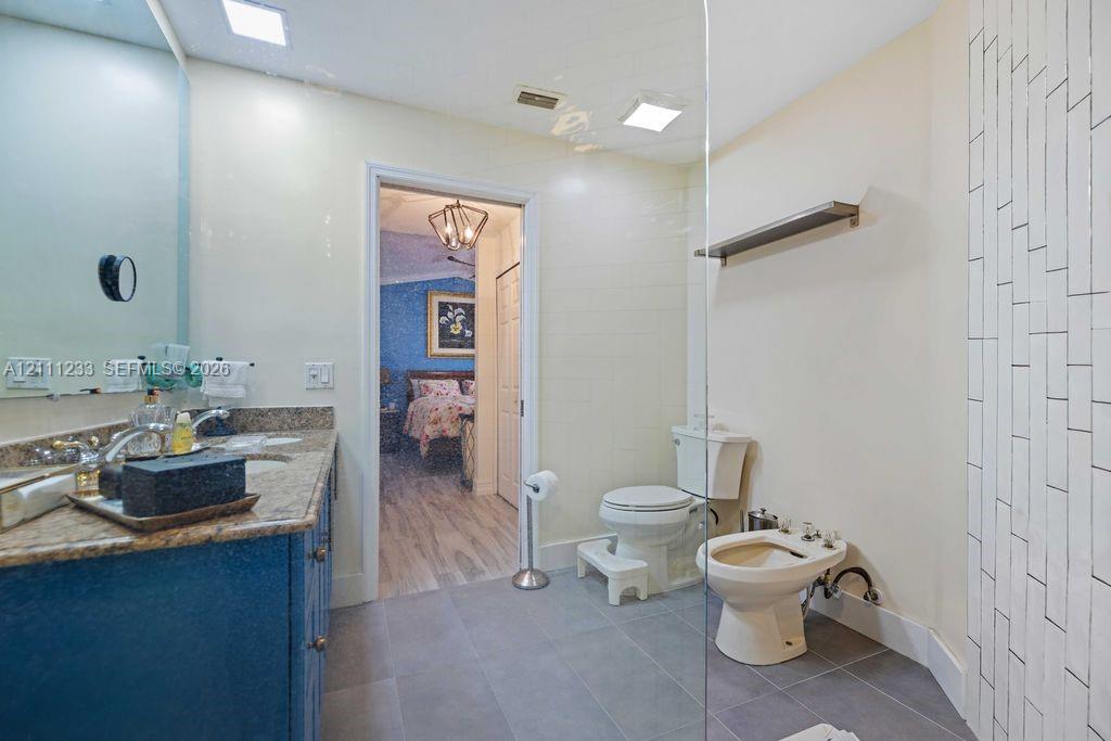 Bathroom featuring a dual-sink vanity with stone-finish countertop, large-format floor tile, and vertical subway tile shower surround