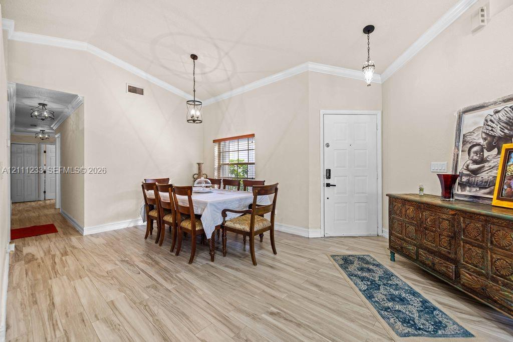 Vaulted ceilings with crown molding, wood-finish flooring, and dual hanging pendant lights