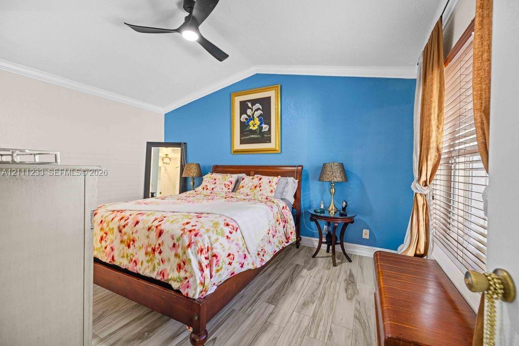 Vaulted ceiling with a matte black modern ceiling fan, wood-finish tile flooring, crown molding, and an accent wall