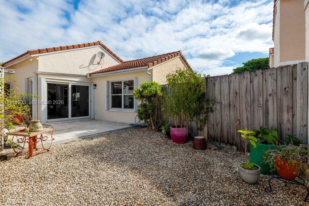 Stucco exterior with a terracotta-style tile roof, sliding glass doors, a stone-paved patio, and a privacy wood fence