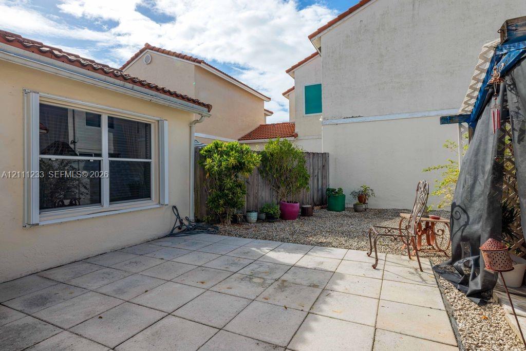 Exterior patio area featuring concrete tile pavers, gravel ground cover, privacy wood fencing, and a stucco-finish building facade