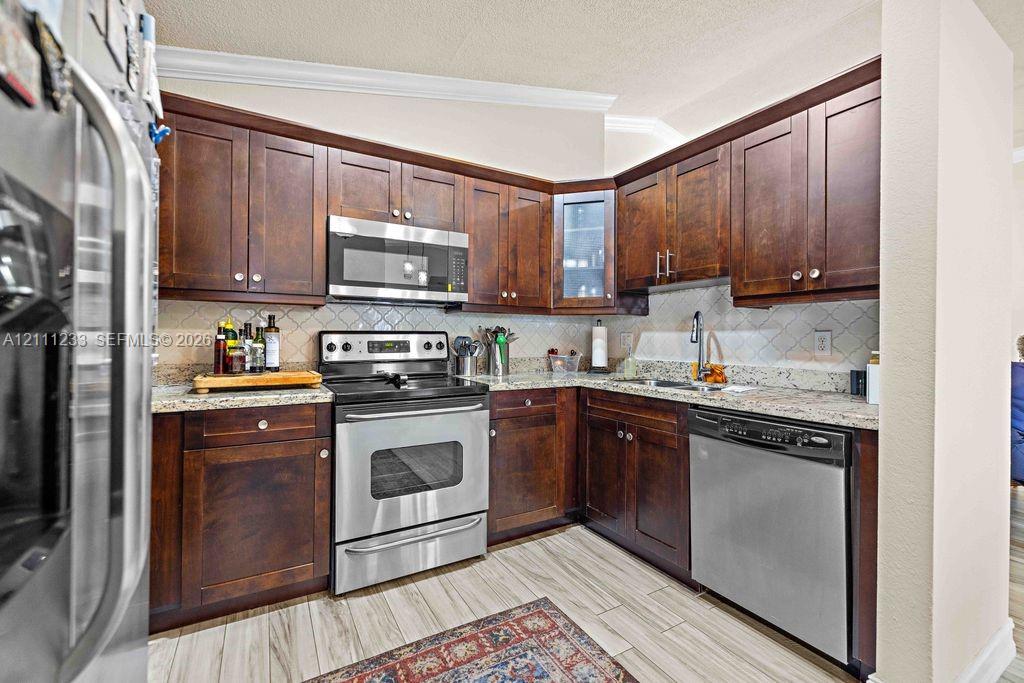 Kitchen featuring dark wood cabinetry, stone countertops, tiled backsplash, stainless steel appliances, and tile flooring Kitchen featuring dark wood cabinetry, stone countertops, tiled backsplash, stainless steel appliances, and tile flooring