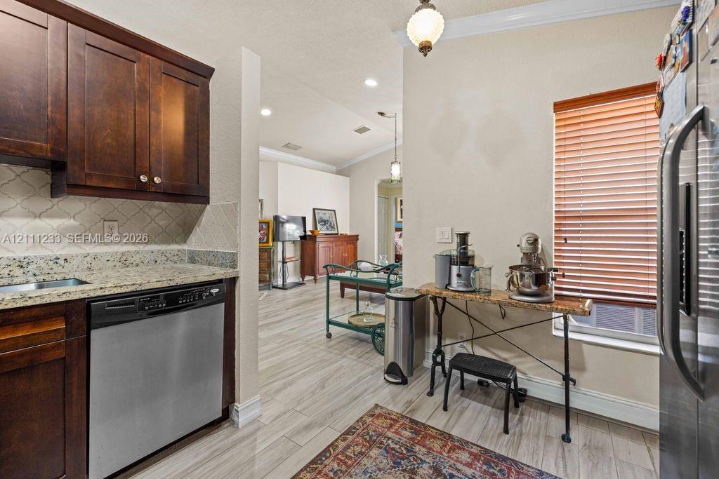 Kitchen featuring dark wood cabinetry, stone countertops, stainless steel dishwasher, arabesque tile backsplash, and wood-finish flooring