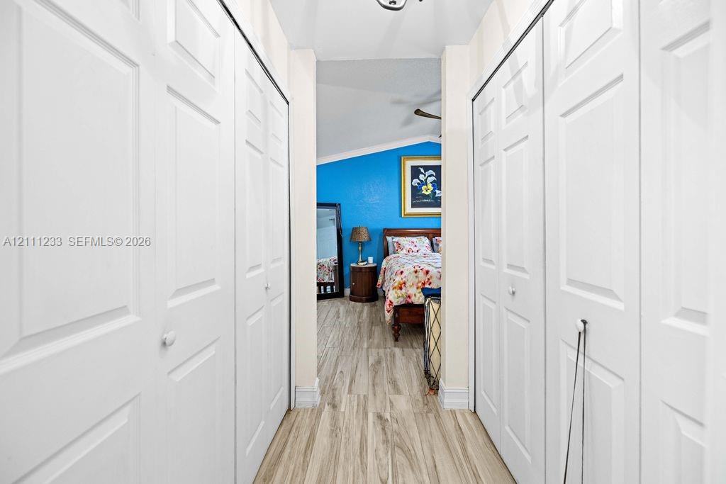 Hallway featuring dual sets of white paneled bifold closet doors and wood-finish flooring