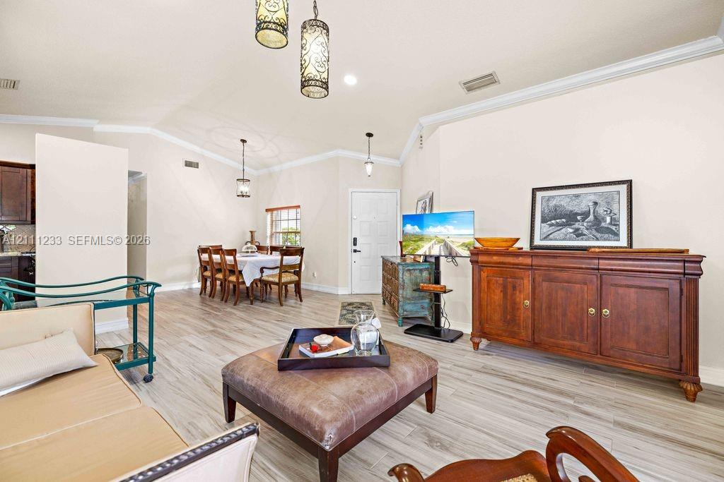Open-concept interior featuring wood-finish flooring, vaulted ceilings with crown molding, and decorative pendant lighting Open-concept interior featuring wood-finish flooring, vaulted ceilings with crown molding, and decorative pendant lighting