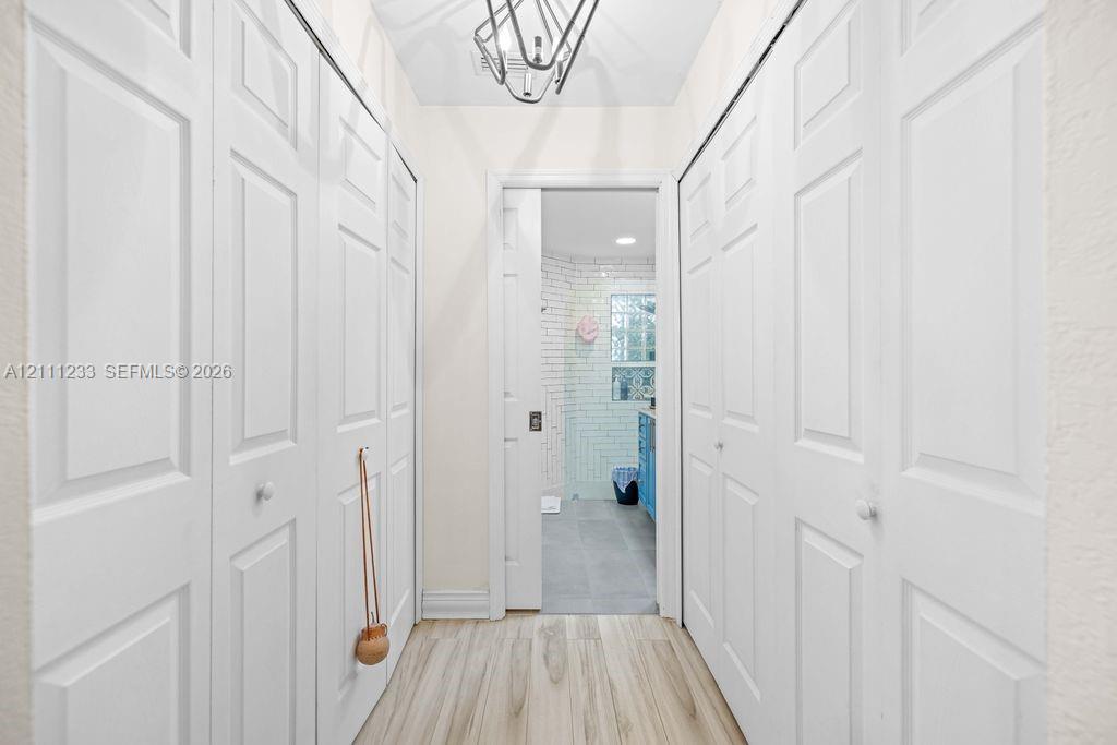 Hallway featuring wood-finish flooring, dual sets of floor-to-ceiling bi-fold closet doors, and a geometric metal pendant light fixture