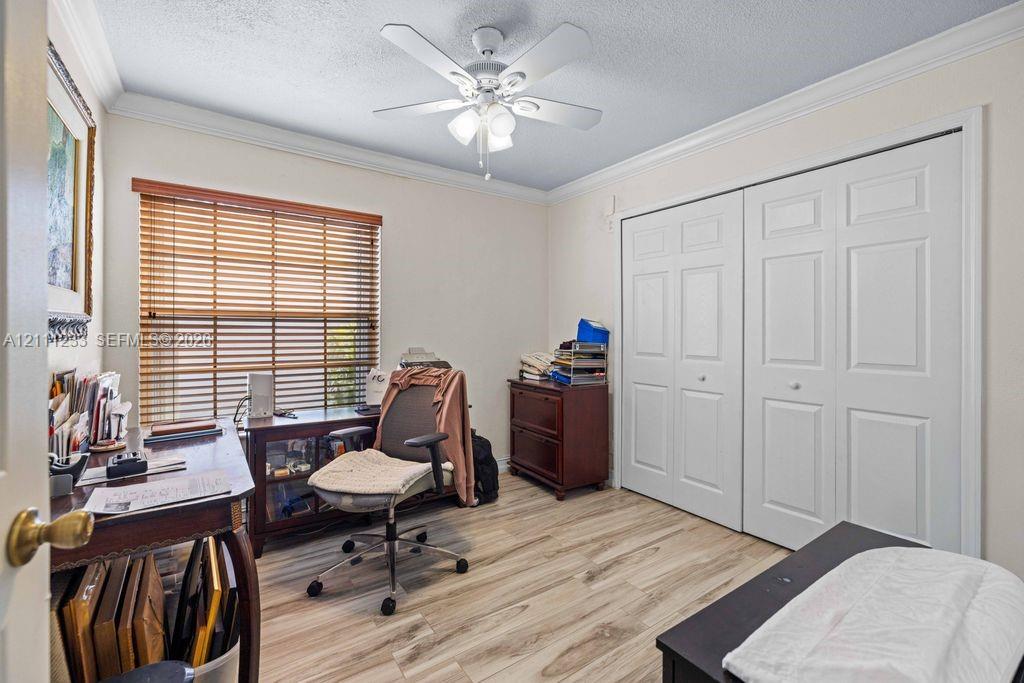 Room featuring wood-finish flooring, crown molding, a ceiling fan with integrated lighting, dual-pane horizontal blinds, and a dual-panel sliding closet