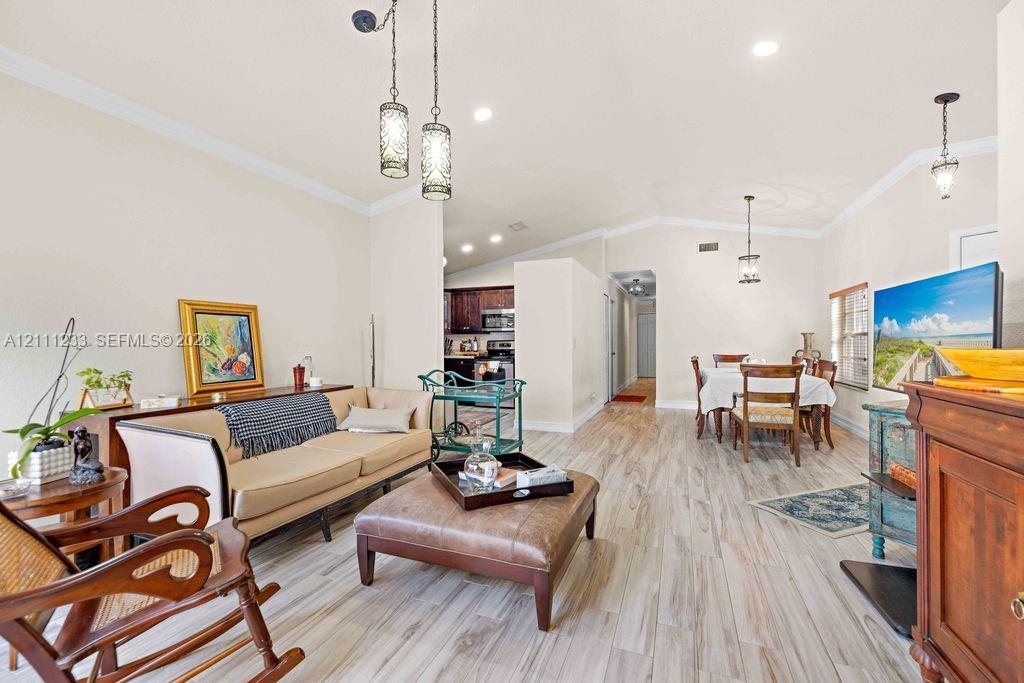 Open-concept interior featuring wood-finish flooring, recessed lighting, crown molding, and decorative pendant fixtures
