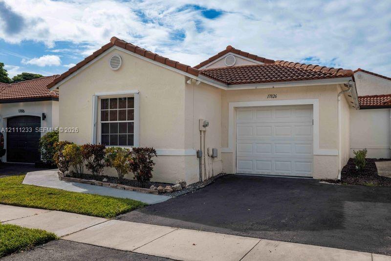 Stucco exterior featuring a terracotta tile roof, single-car garage, and established landscape beds Stucco exterior featuring a terracotta tile roof, single-car garage, and established landscape beds