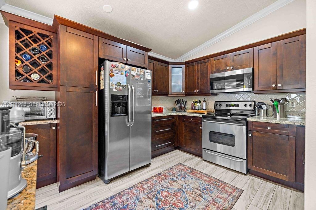 Kitchen featuring dark wood cabinetry, built-in wine rack, stone countertops, stainless steel appliances, and wood-finish tile flooring Kitchen featuring dark wood cabinetry, built-in wine rack, stone countertops, stainless steel appliances, and wood-finish tile flooring