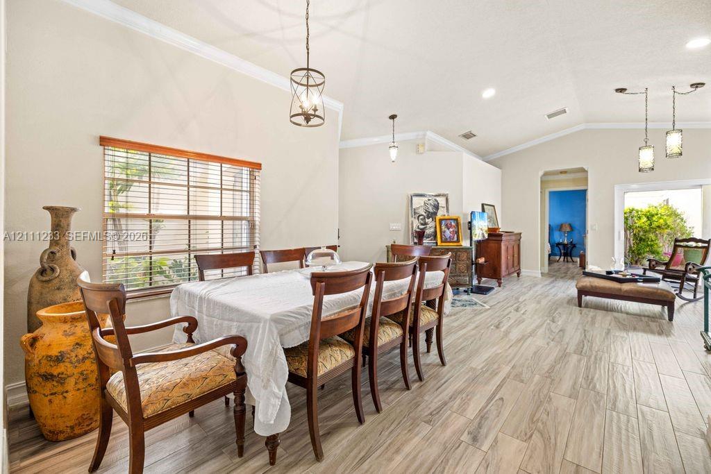 Open-concept dining area featuring vaulted ceilings, wood-finish tile flooring, crown molding, and multiple multi-light pendant fixtures Open-concept dining area featuring vaulted ceilings, wood-finish tile flooring, crown molding, and multiple multi-light pendant fixtures