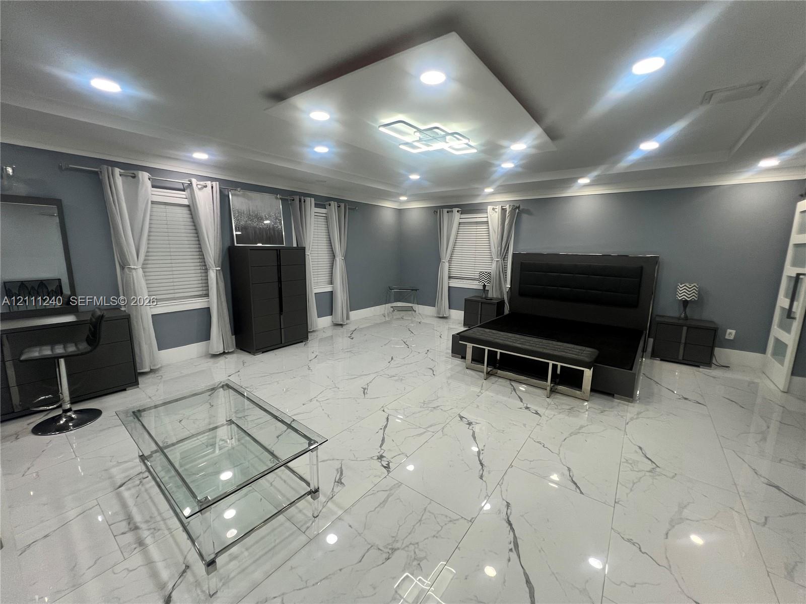 Large-format tile flooring with veining, recessed ceiling lighting, a tiered central ceiling fixture, and multiple windows