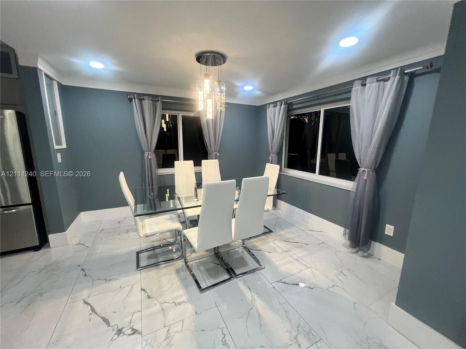Large-format rectified tile flooring with a marble-finish aesthetic, modern multi-pendant light fixture, recessed ceiling lighting, and dual windows