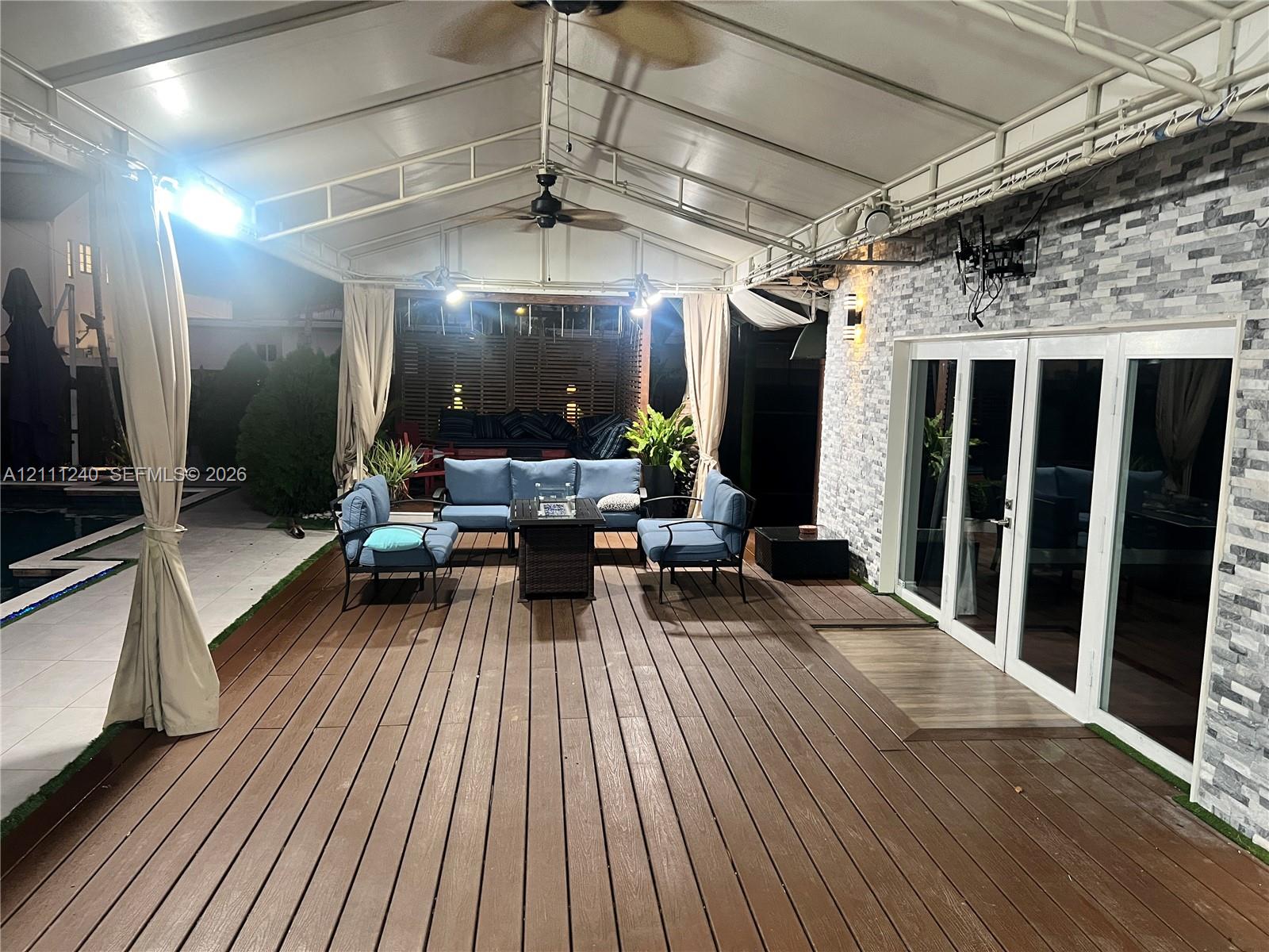 Covered patio featuring a wood-finish deck, stacked stone exterior wall, ceiling-mounted fans, and multi-panel glass doors