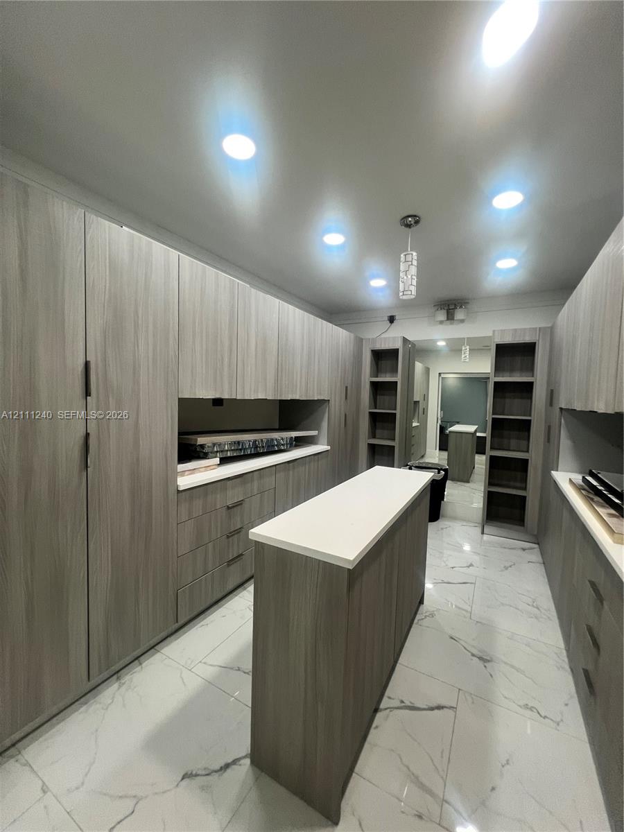 Custom cabinetry featuring wood-finish veneer, integrated central island with solid-surface countertop, recessed ceiling lighting, and large-format porcelain tile flooring